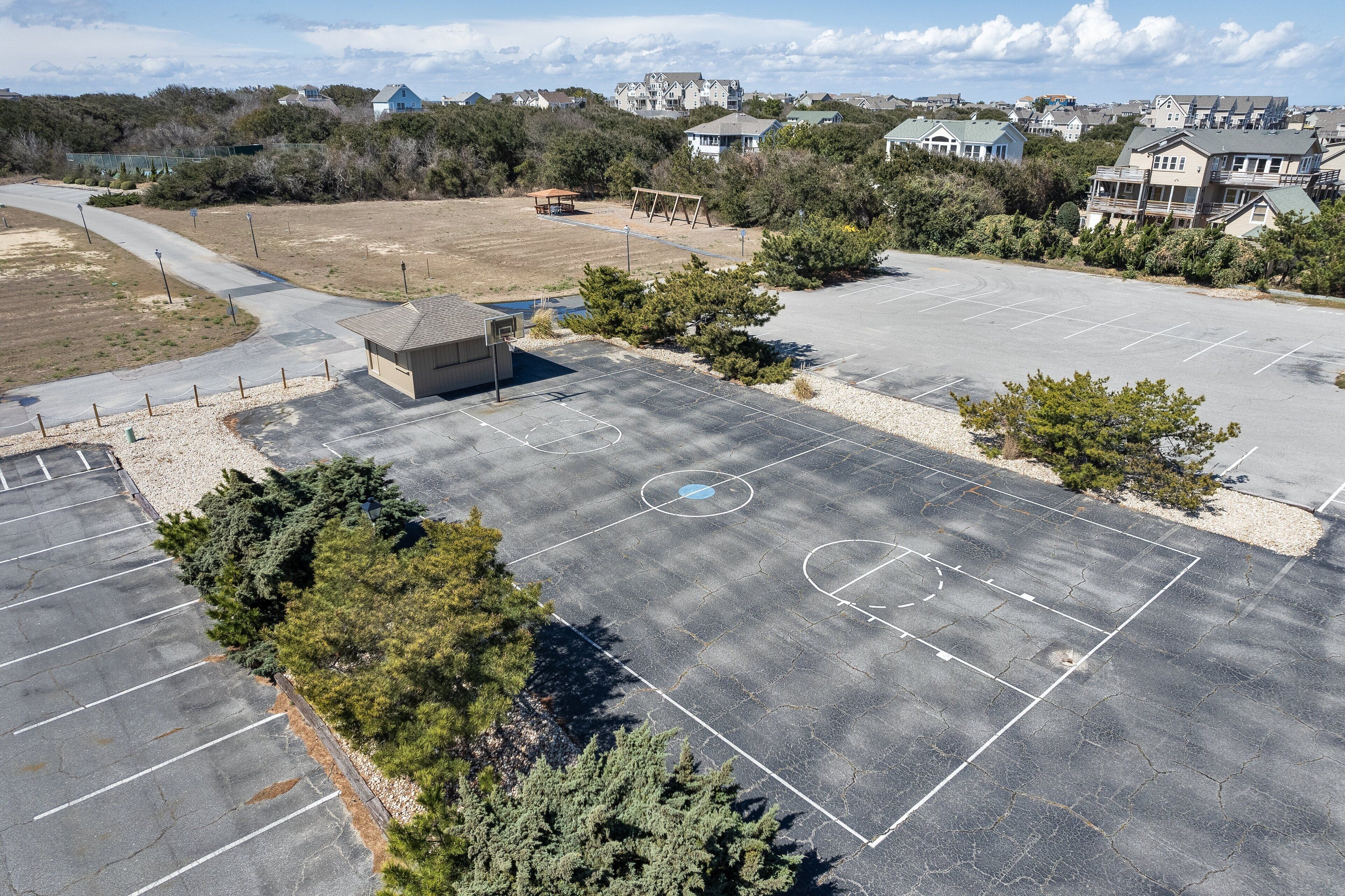 An aerial view of a parking lot with basketball courts, surrounded by trees and residential buildings.