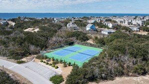 Un court de tennis entouré d’une végétation luxuriante et de bâtiments résidentiels.
