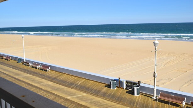 Uitzicht op het strand vanaf een balkon met houten vloer, bankjes en een hekwerk.