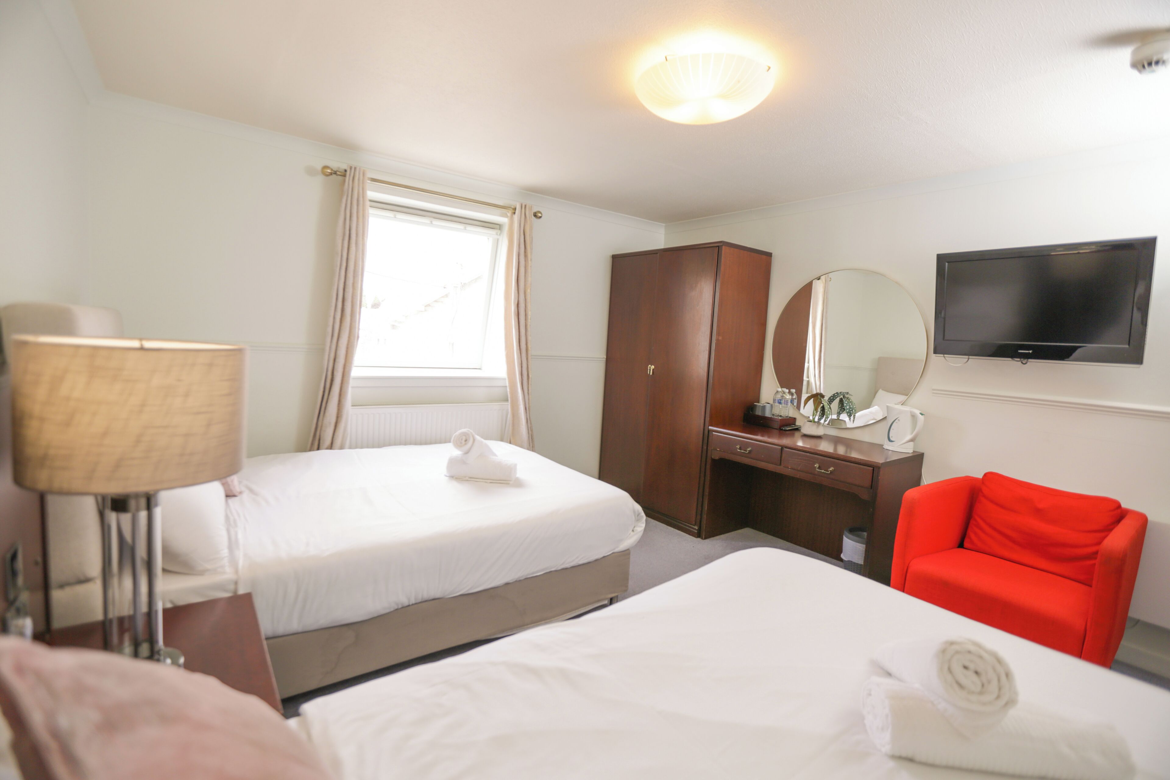 A hotel room with two beds, a desk, a chair, a television, and a window with curtains.