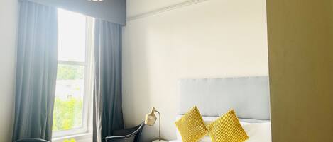 A hotel room with a bed, two chairs, a lamp, and a window with curtains.