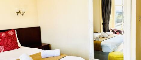 A hotel room with a large bed, a wooden headboard, a mirror, and a yellow ottoman.