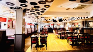 Un restaurante con techo cubierto de discos de vinilo, mesas y sillas de madera, y un letrero de Coca-Cola al fondo.
