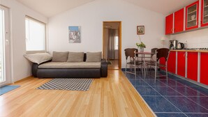 A compact living space with a sofa, dining table, chairs, a kitchen with red cabinets, and a hallway leading to another room. - Amazing apartment in Nin with WiFi (Nin)