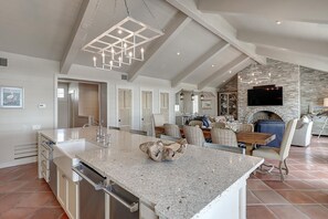 A spacious kitchen with a large island, a dining area with a fireplace, and a living room with a stone wall and a flat-screen TV. - Gulf-Front Home, Panoramic Views, Resort-Style Amenities in Cinnamon Shore (Port Aransas)