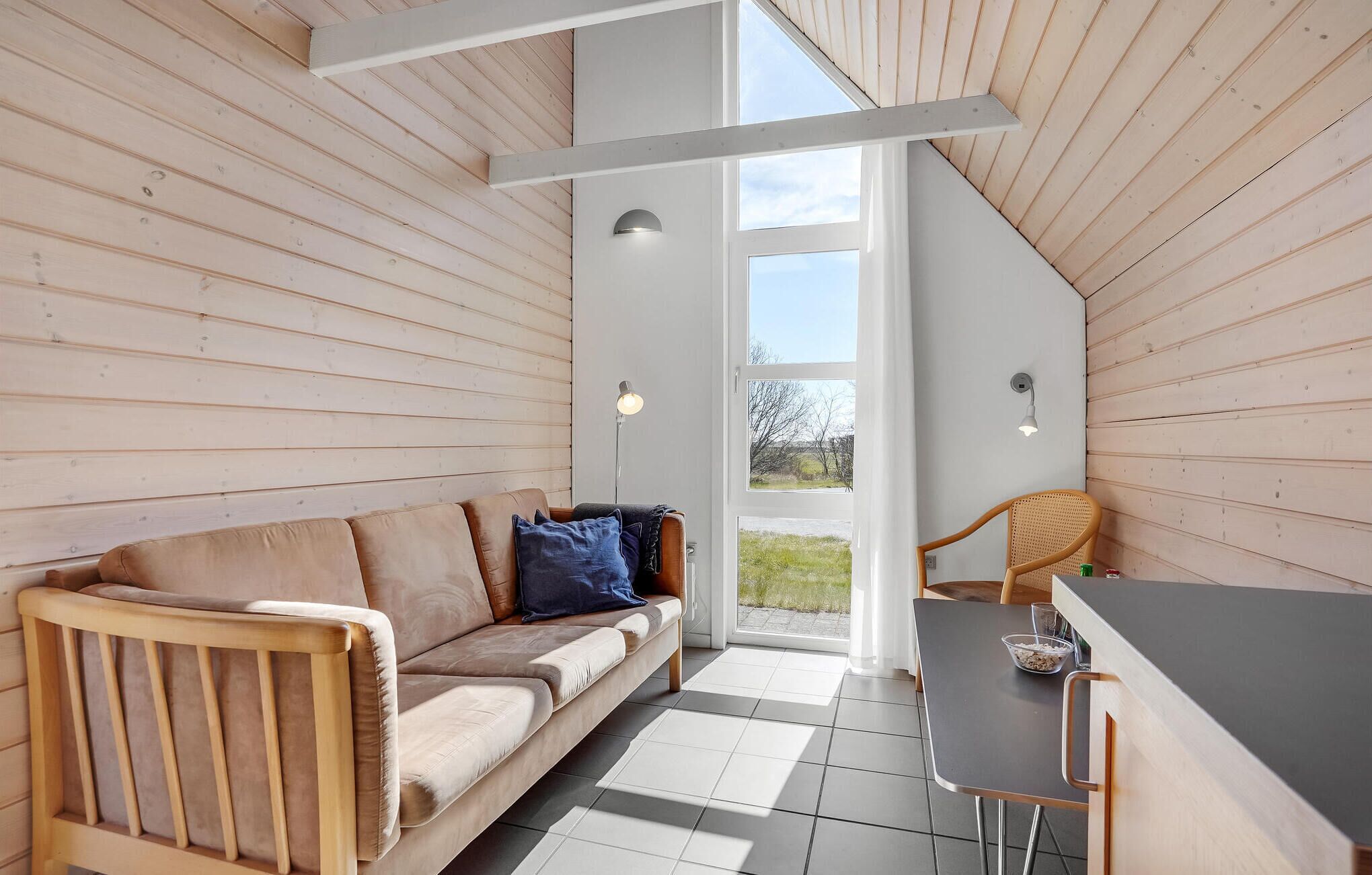 Et hyggeligt rum med trælofter, en sofa, et spisebord og en stol.
