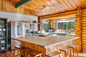 A log cabin interior with a central island, wooden bar stools, a refrigerator, a microwave, and a sink.