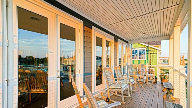 A covered outdoor deck with wooden chairs and tables, large sliding glass doors, and a view of the marina. - Simply The Best - At Angler's Nest! (Lewes)