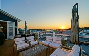 A deck with outdoor seating and a view of a marina at sunset.