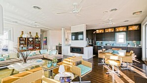 A spacious living area with a sofa, coffee table, and wicker chairs. There is a fireplace, kitchen area with a dining table, and a ceiling fan. - Simply The Best - At Angler's Nest! (Lewes)