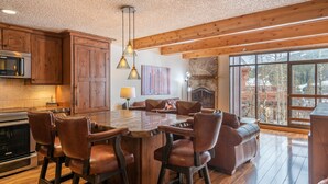 A spacious kitchen with wooden cabinets, a large island with bar stools, a stone fireplace, and a view of the outdoors. - Perfect view of Super Bee, ski-in/out, wonderful sunlight, free WiFi, parking (Copper Mountain)