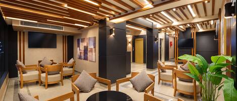 A modern lounge area with wooden furniture, a round black table, and a large potted plant.