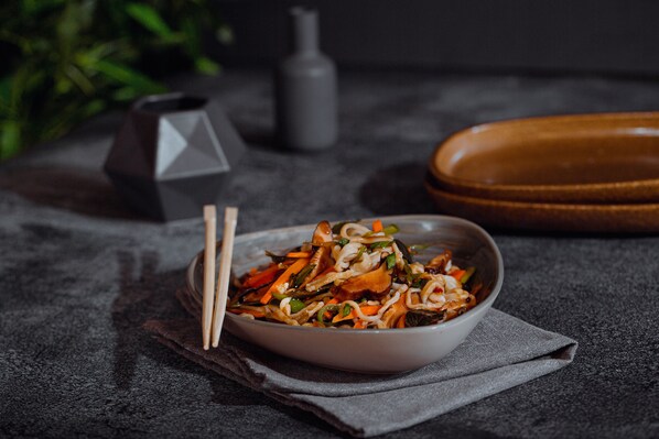 A bowl of stir-fried noodles with vegetables on a dark textured surface. - Stay Inn Cairo Hotel (Giza)