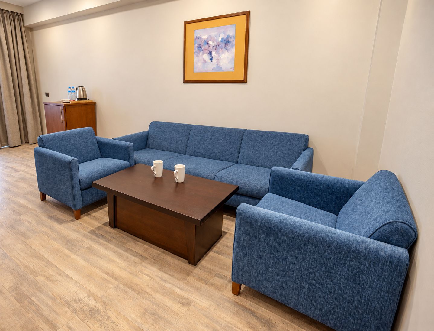 A room with a blue sofa set, a wooden coffee table, and a framed artwork on the wall.