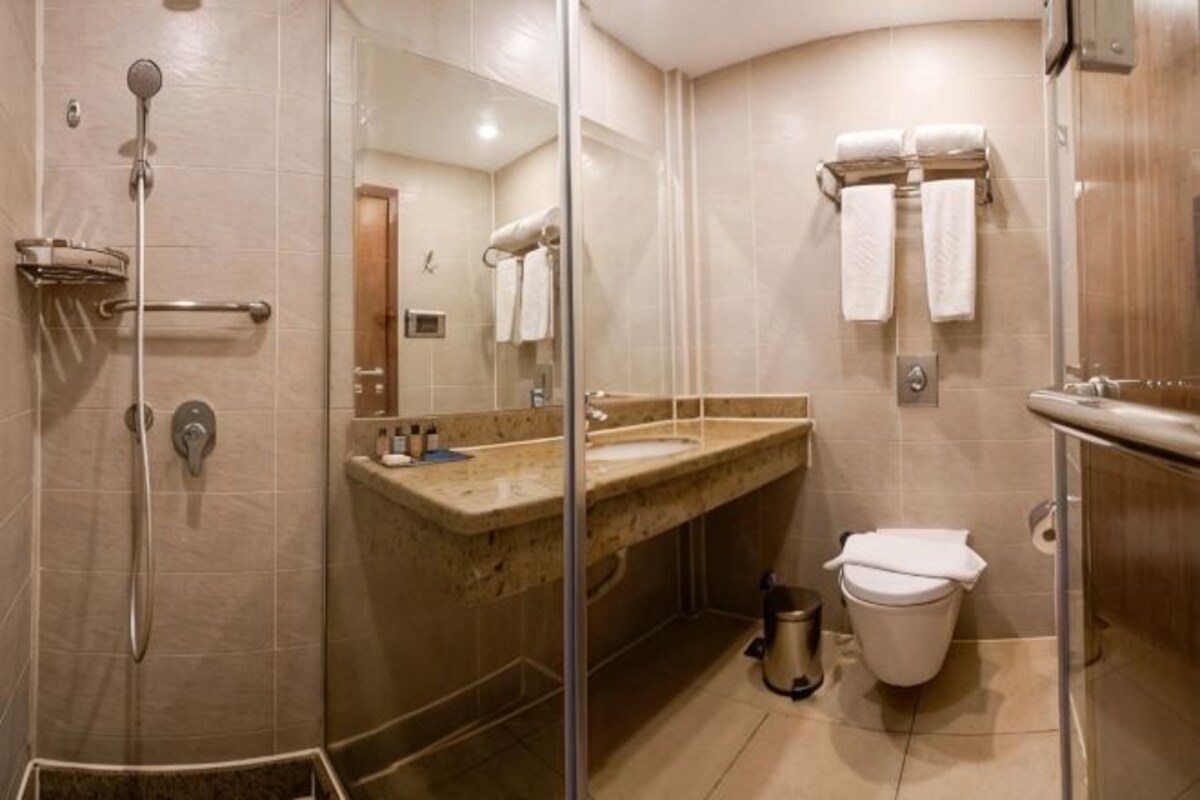 Une salle de bain d’hôtel avec une douche en verre, un lavabo avec un miroir et des toilettes.