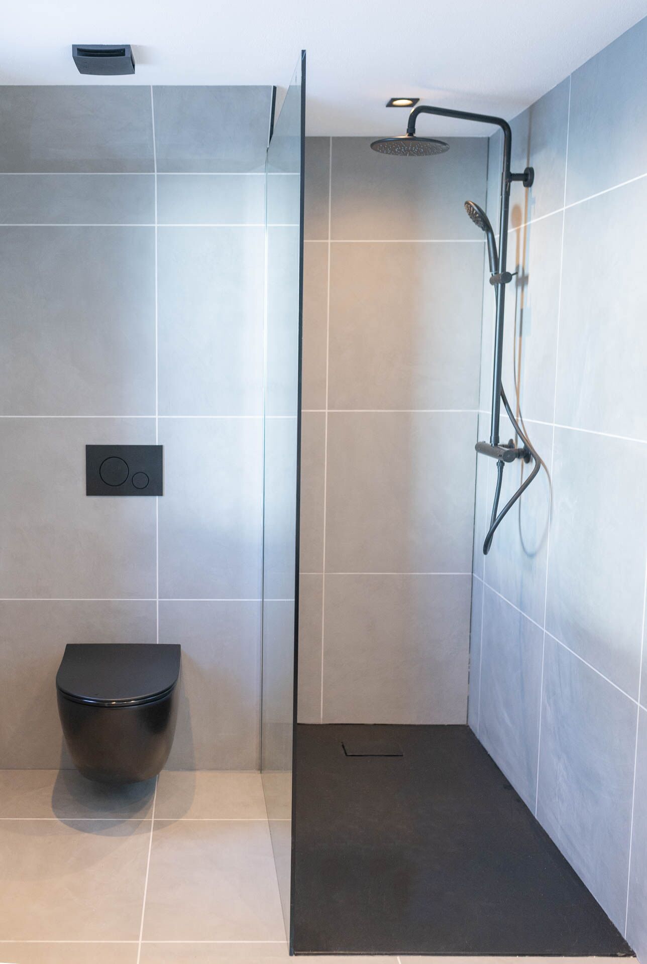 Ein modernes Badezimmer mit einer Duschkabine, einer schwarzen Toilette und gefliesten Wänden.
