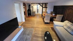 A cozy living room with a fireplace, a sofa, and a dining area with chairs. - Apartment with garden at the foot of the Säntis (Urnäsch)