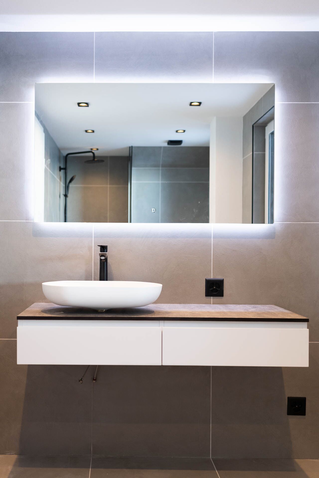 Een moderne badkamer met een grote rechthoekige spiegel, een witte wastafel en inbouwspots.