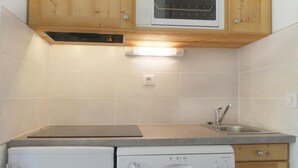 A compact kitchen with wooden cabinets, a built-in microwave, a sink, and a dishwasher.