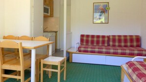 A compact room with a dining table and chairs, a sofa, and a kitchenette.