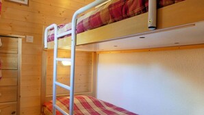 A bunk bed room with a ladder, wooden walls, and a small dresser.