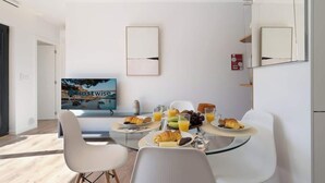 Un'area pranzo moderna con tavolo in vetro, sedie bianche e un'impostazione per la colazione con cornetti, uva e succo d'arancia.