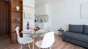 Un soggiorno moderno con un tavolo da pranzo in vetro, sedie bianche, un divano grigio e mensole in legno.