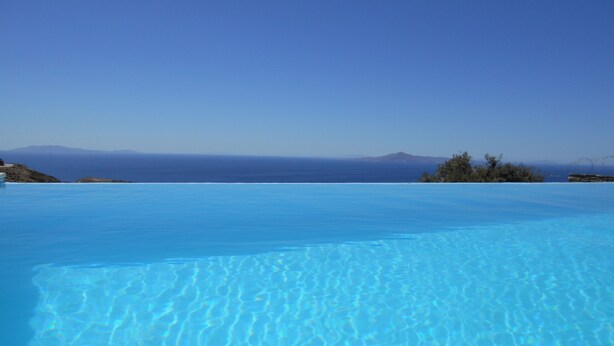 Uma piscina infinita azul límpida com vista para o oceano e montanhas ao longe.