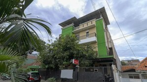 Ein mehrgeschossiges Wohngebäude mit grüner und beiger Fassade, einem verschlossenen Eingang und einem geparkten Auto davor.