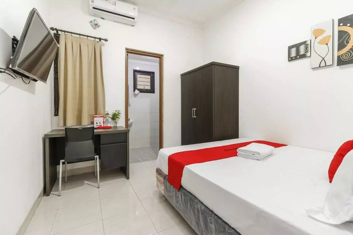 Une chambre d’hôtel équipée d’un lit, d’un bureau, d’une armoire et d’un téléviseur fixé au mur.