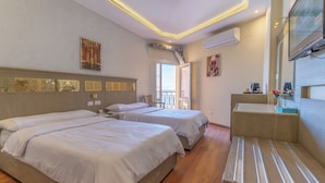 A hotel room with two beds, a wooden bench, a TV, and a balcony with a view.