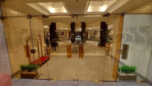 A hotel lobby with a glass entrance, a reception desk, and a seating area with chairs and tables.