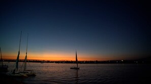A calm body of water at dusk with several sailboats and a distant city skyline. - Lotus Luxor Hotel (Luxor)