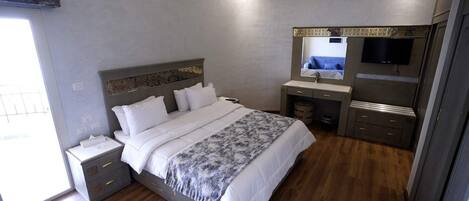 A modern bedroom with a large bed, bedside tables, a vanity with a mirror, and a TV.