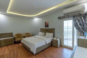 A hotel room with a bed, two armchairs, a desk, and a balcony with a railing.