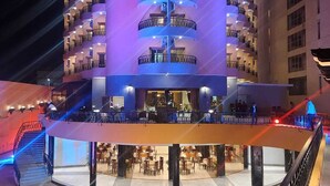 A multi-story hotel with balconies, a covered outdoor seating area, and a staircase leading to the entrance.