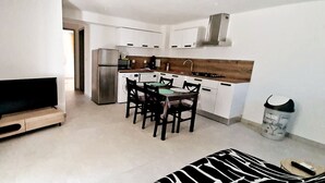 A modern kitchen with white cabinets, a stainless steel refrigerator, and a dining area with a table and chairs. - T3 with pool 2mn from the beach (Pietracorbara)