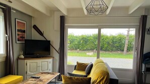 A modern living room with a sofa, a coffee table, a television, and a view of a garden through a sliding door. - Charming house 800m from the sea and Ménéham (Kerlouan)