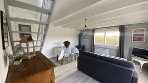 A spacious living area with a high ceiling, a dark-colored sofa, a dining table with chairs, and a staircase. - Charming house 800m from the sea and Ménéham (Kerlouan)