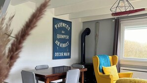 A dining area with a wooden table and chairs, a yellow armchair, and a decorative wall sign. - Charming house 800m from the sea and Ménéham (Kerlouan)