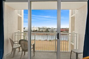 Enjoy the serene view of the water from this balcony, featuring two comfortable chairs and a small table.