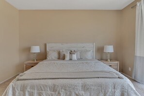 Une chambre à coucher avec un grand lit, deux tables de chevet avec des lampes et une palette de couleurs neutres.