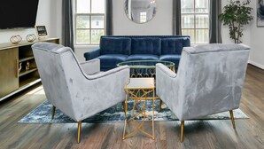 A modern living room with a blue sofa, two grey armchairs, a gold-framed coffee table, a large mirror, and a unique ceiling light fixture. - Condo in Midtown. One block from downtown. Minutes from Texas Medical Center  (Houston)