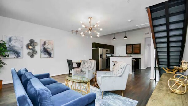 A modern living room with a blue sofa, a round coffee table, and a dining area with a white table and chairs. There is a kitchen in the background with a microwave and cabinets. - Condo in Midtown. One block from downtown. Minutes from Texas Medical Center  (Houston)
