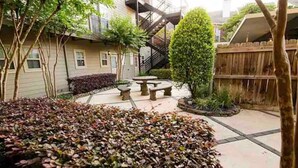 A courtyard with a stone table, a wooden fence, and a staircase leading to an upper level. - Condo in Midtown. One block from downtown. Minutes from Texas Medical Center  (Houston)