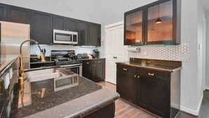 A modern kitchen with dark cabinets, a stainless steel refrigerator, a microwave, and a large island with a sink. - Condo in Midtown. One block from downtown. Minutes from Texas Medical Center  (Houston)