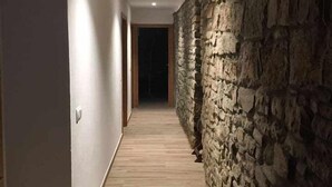 A hallway with a wooden floor, white walls, and a stone wall on one side. - Casa Mestres - La Botiga (Pujalt)