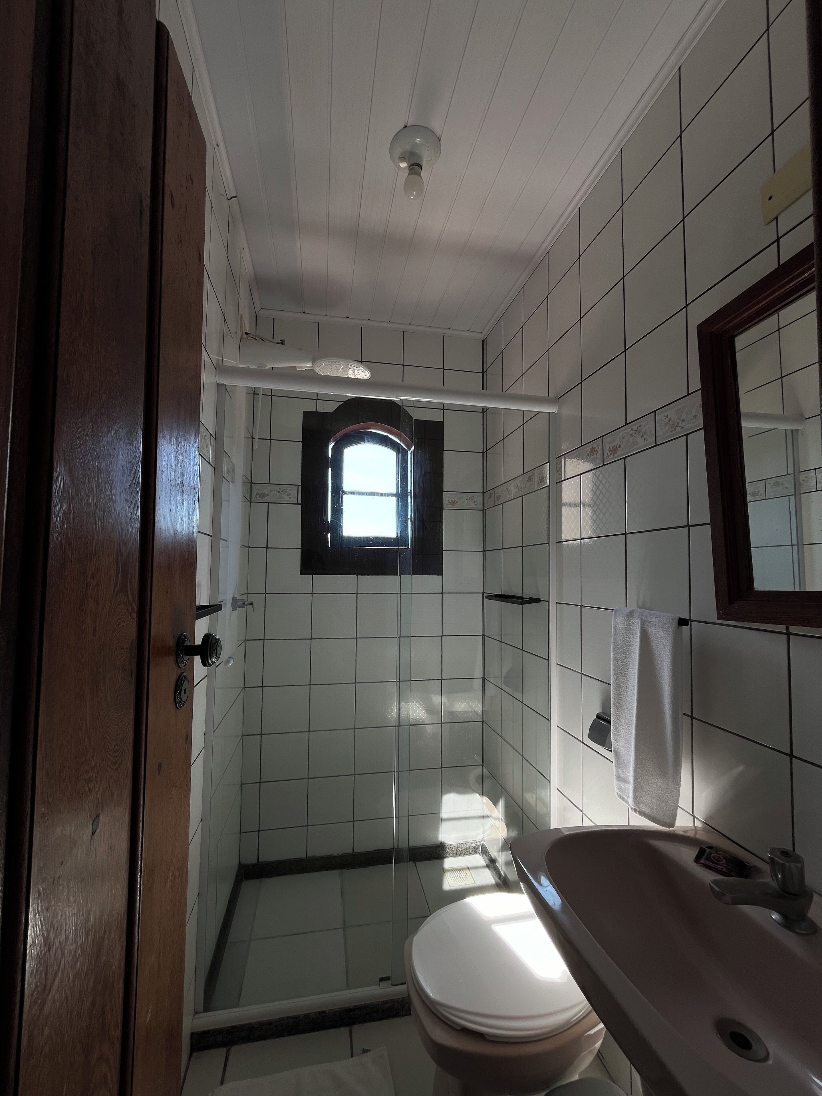 A bathroom with white tiled walls, a window, a toilet, and a sink.
