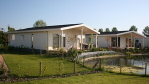 Une maison mobile blanche, dotée d’un patio couvert et d’un petit étang dans le jardin.