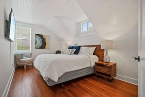 A bedroom with a sloped ceiling, a bed with white bedding, a nightstand with a lamp, and a painting on the wall. - Stay in A Castle In St. Augustine, Hot Tub, Fireplace (St. Augustine)